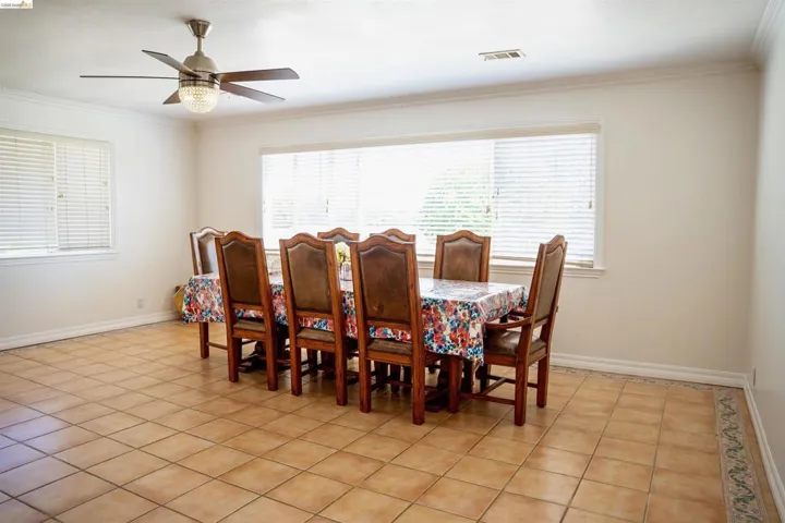 Bright interior space featuring a large window, tiled flooring, crown molding, and a ceiling fan with integrated lighting