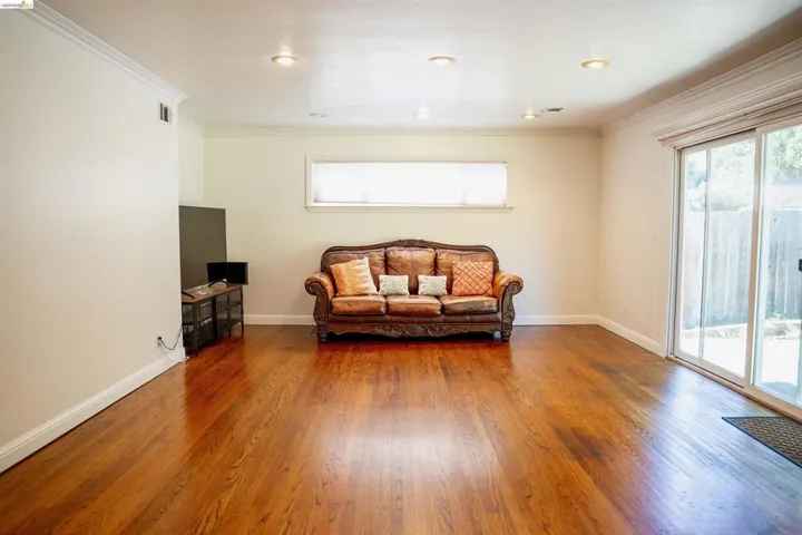 Spacious room featuring hardwood flooring, recessed lighting, crown molding, a large sliding glass door, and an additional window
