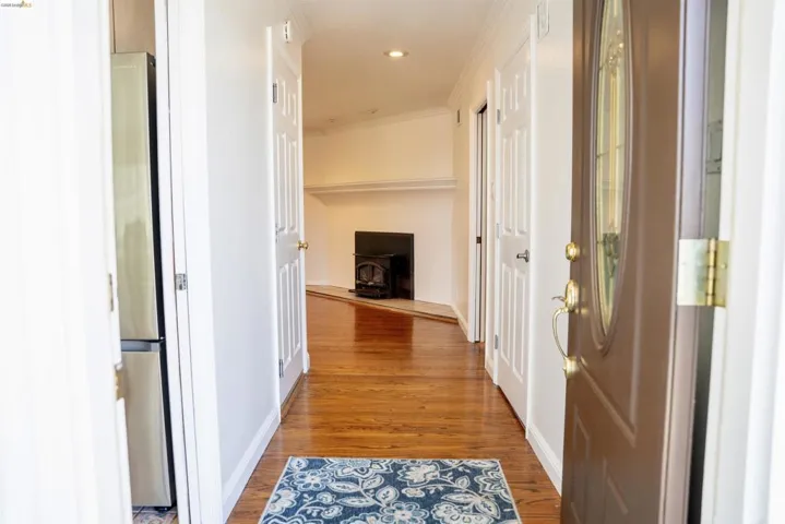 Entryway featuring a wood-finish floor, an oval lite entry door, white trim, a recessed ceiling light, and a black wood-burning stove