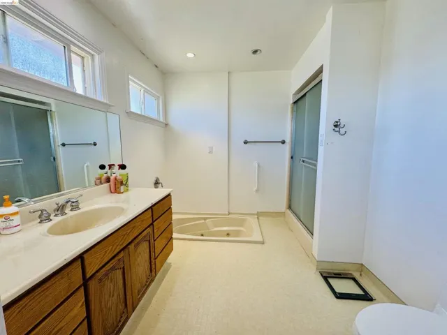 Bathroom featuring a built-in jetted tub, a separate shower with sliding frosted glass doors, and a wood-finish vanity with an integrated sink and light-toned countertop