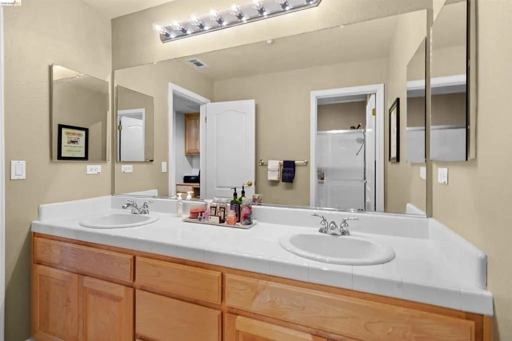 Double vanity featuring two oval sinks with chrome fixtures, a tile-finish countertop, and natural wood cabinetry