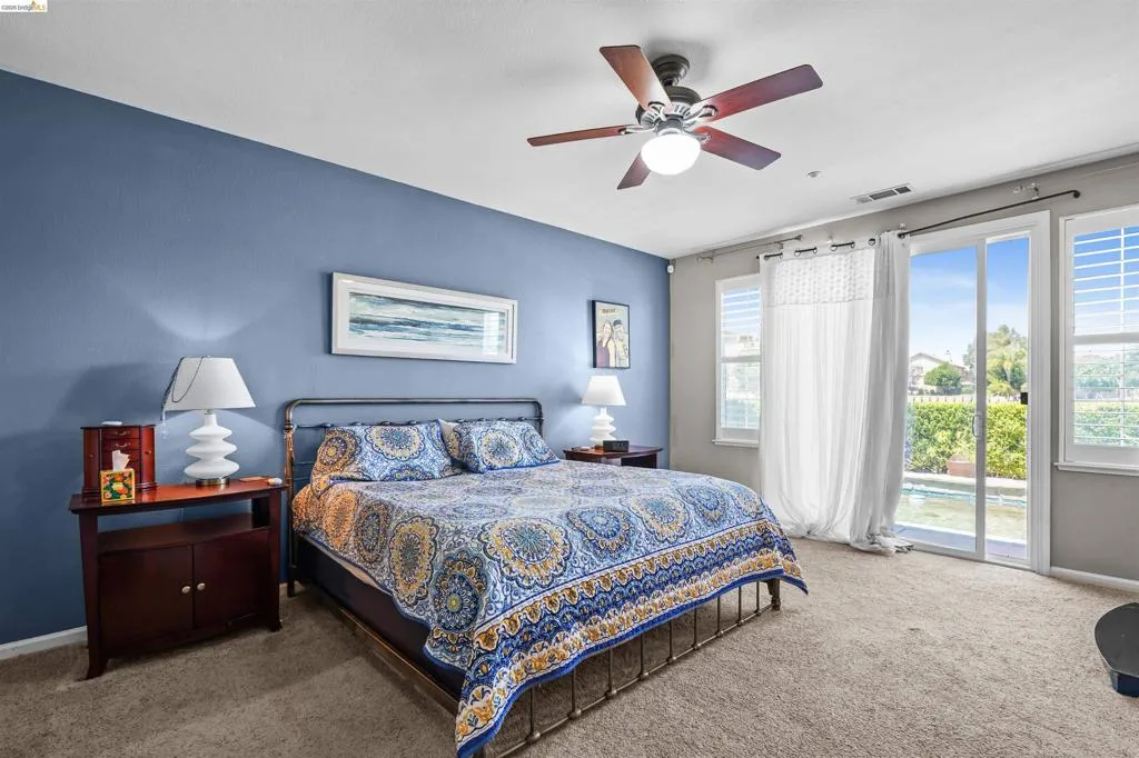 Spacious room featuring a sliding glass door, dual windows with plantation shutters, a ceiling fan, and carpeted flooring