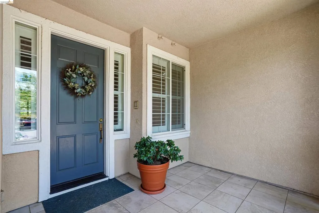 Covered entryway featuring a paneled door with sidelights, a window with plantation shutters, stucco exterior, and tiled flooring