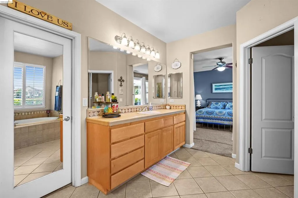 Bathroom featuring a dual vanity with light wood cabinetry, a large wall mirror, and a multi-bulb light fixture