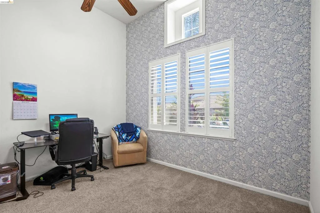 Vaulted ceiling room featuring a decorative accent wall, white window shutters, and a high transom window