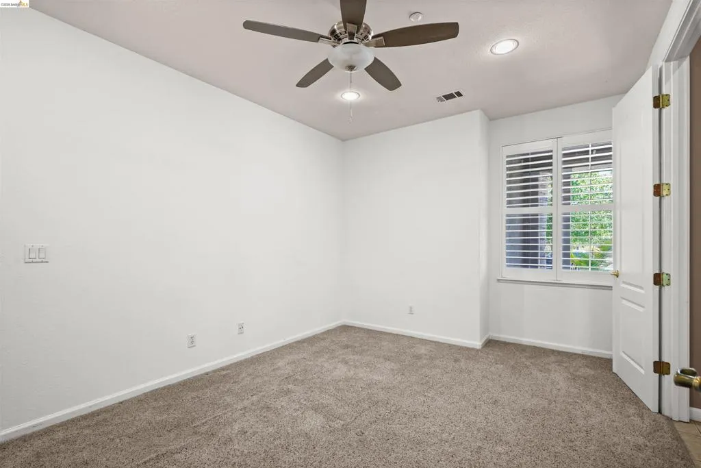 Carpeted room featuring a ceiling fan, recessed lighting, and a window with plantation shutters