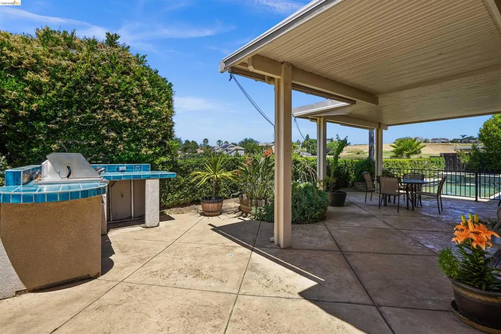 Expansive patio featuring a built-in outdoor grill with tiled countertops, a covered seating area, and concrete hardscaping