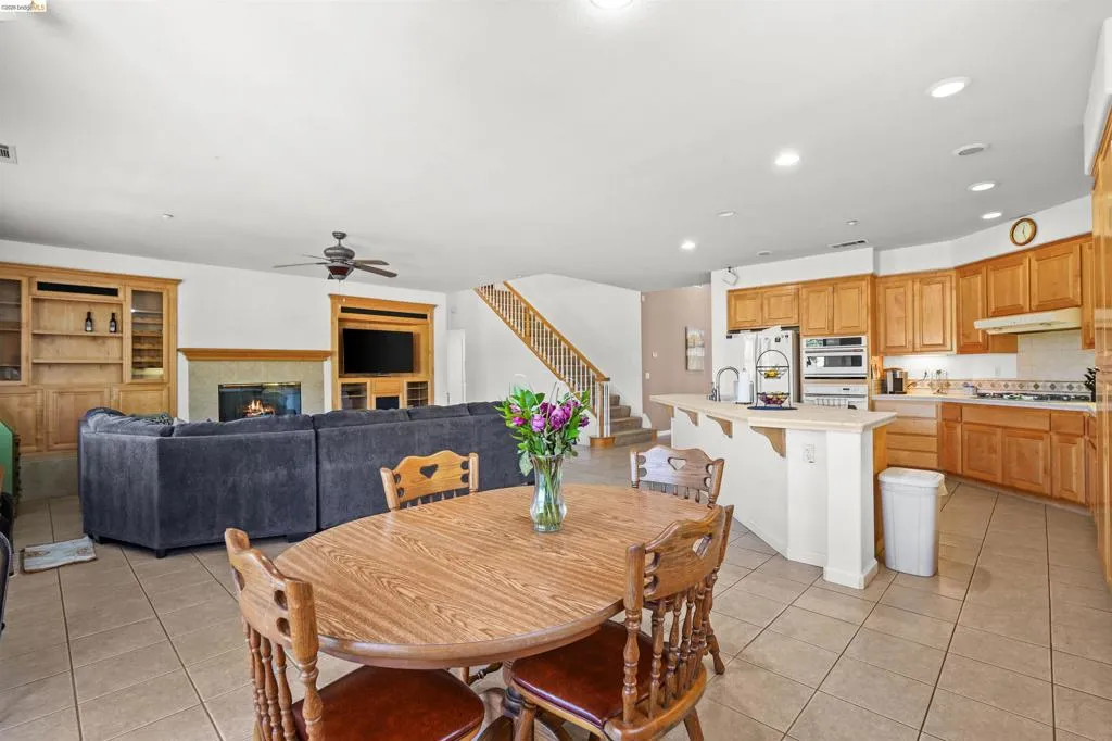 Open-concept living space featuring a gas fireplace with stone surround, built-in shelving, wood-finish cabinetry, a breakfast bar, and tile flooring
