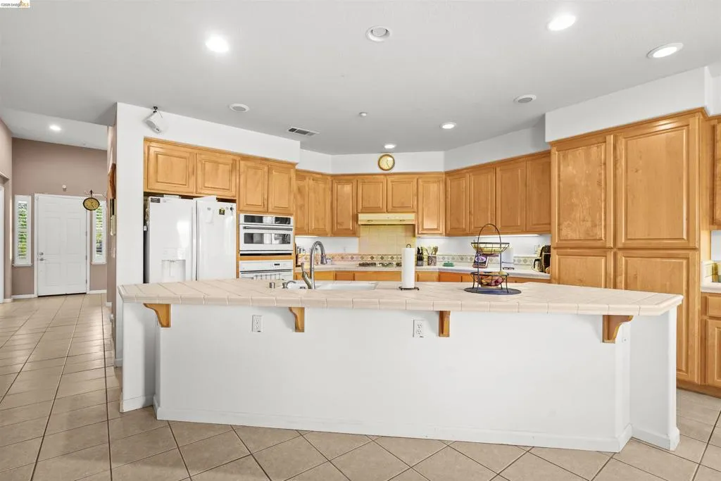 Kitchen featuring light wood cabinetry, white appliances, recessed lighting, a tile backsplash, and a large island with a tile countertop