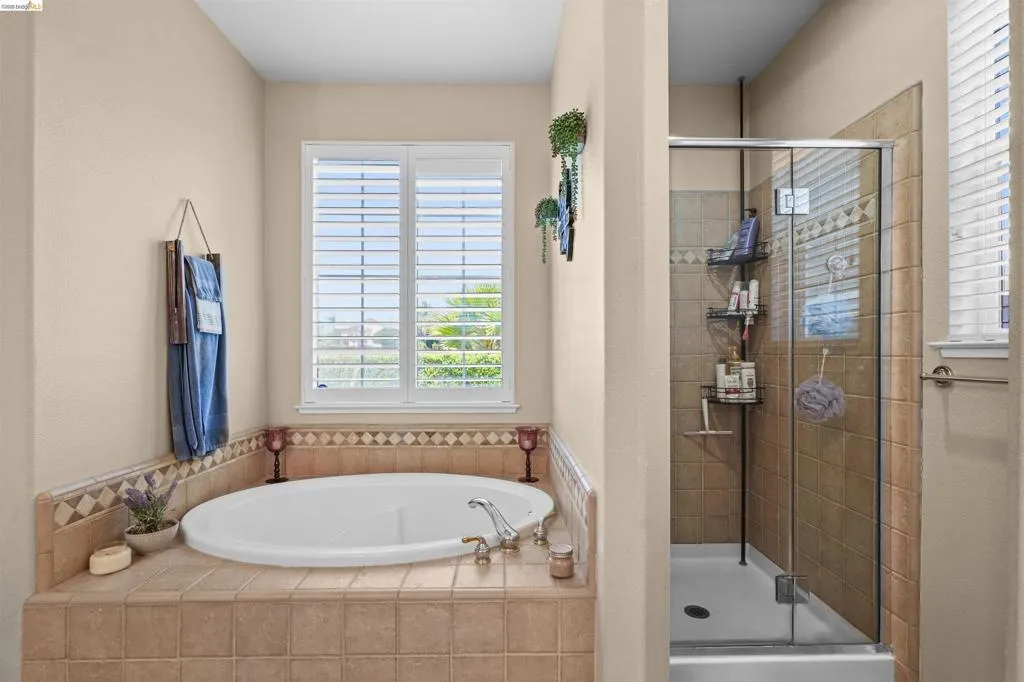 Recessed bathtub with tile surround and decorative border, accompanied by a separate glass-enclosed shower featuring tile walls