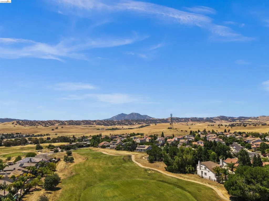 Aerial perspective showcasing a residential community bordered by a golf course, expansive natural landscapes, and distant mountains