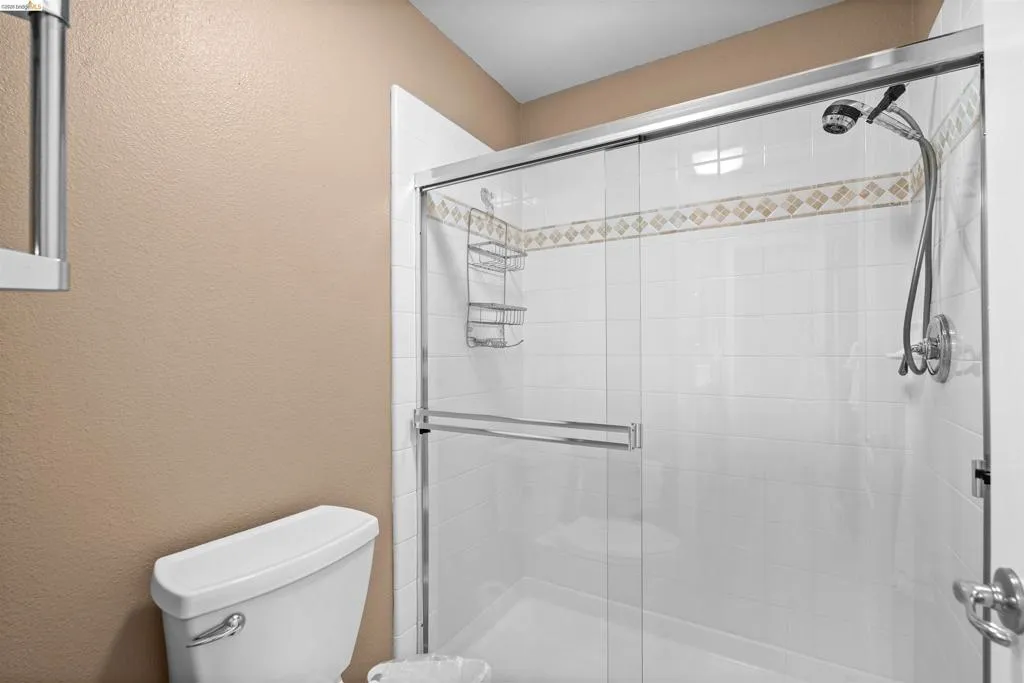 Shower enclosure featuring a chrome-framed sliding glass door, white tile surround, decorative tile accent band, and a multi-function shower head