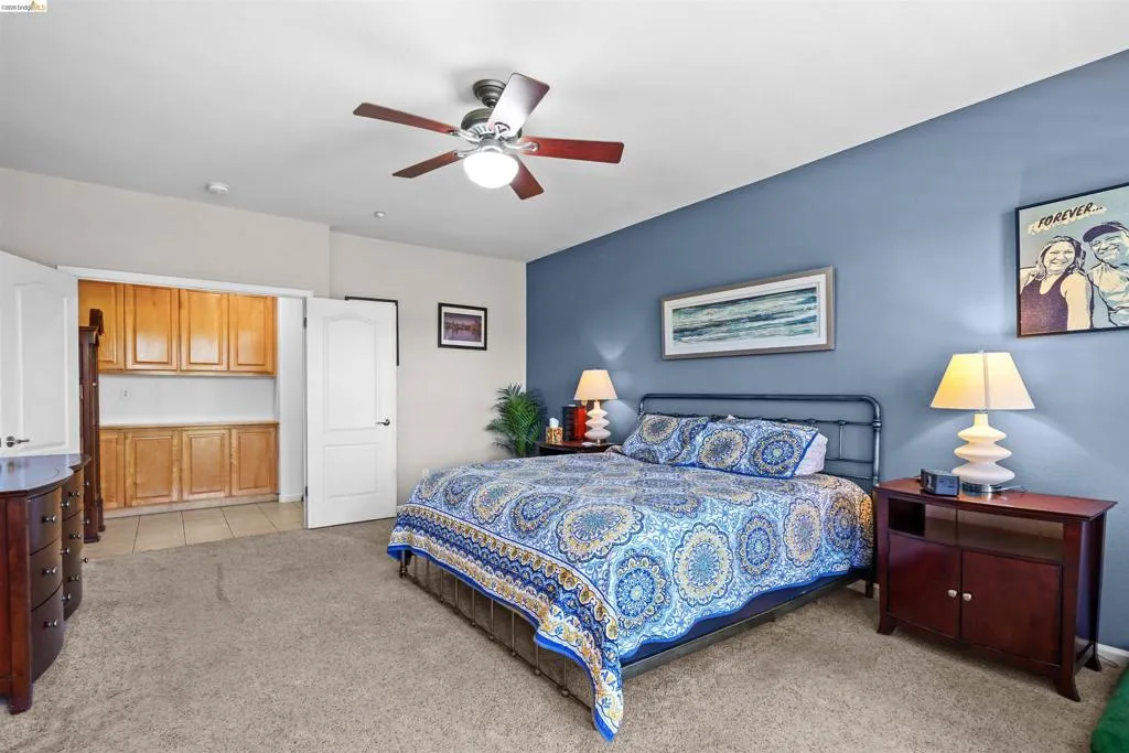 Spacious room featuring a ceiling fan with integrated lighting, a dedicated storage area with wood cabinetry, and a full-height door