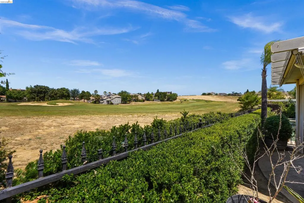 Expansive golf course terrain bordered by a manicured hedge and a decorative wrought iron fence
