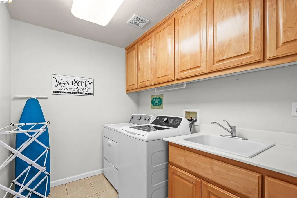 Functional laundry area featuring light wood cabinetry, a built-in utility sink with a chrome faucet, light-toned countertops, and tiled flooring
