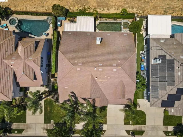 Aerial view showcasing a tiled roof, front yard landscaping, and paved driveway