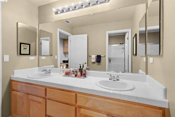 Double vanity featuring two oval sinks with chrome fixtures, a tile-finish countertop, and natural wood cabinetry