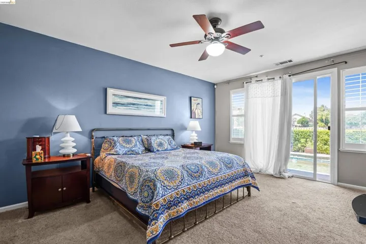 Spacious room featuring a sliding glass door, dual windows with plantation shutters, a ceiling fan, and carpeted flooring