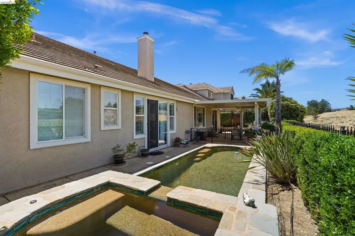 Rear exterior featuring a rectangular pool with an integrated spa, stone coping, and a covered patio area