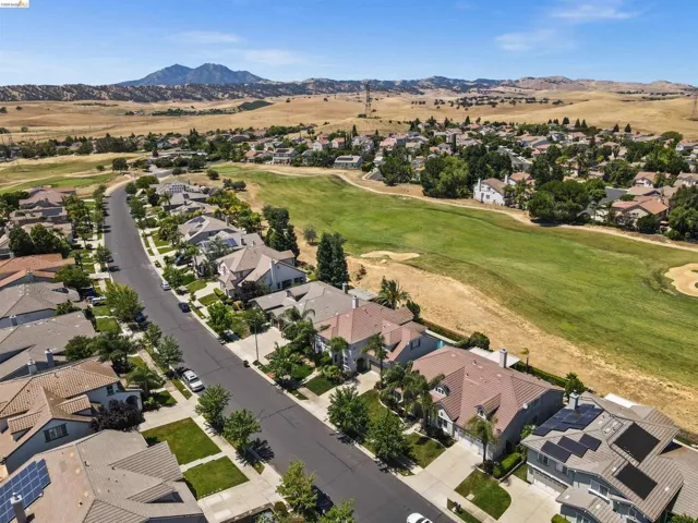 Residential neighborhood featuring a paved street, mature trees, manicured lawns, and golf course access