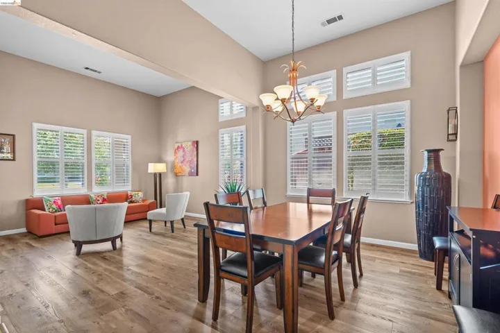 Open-concept living and dining area featuring vaulted ceilings, wood-finish flooring, and multiple windows with plantation shutters