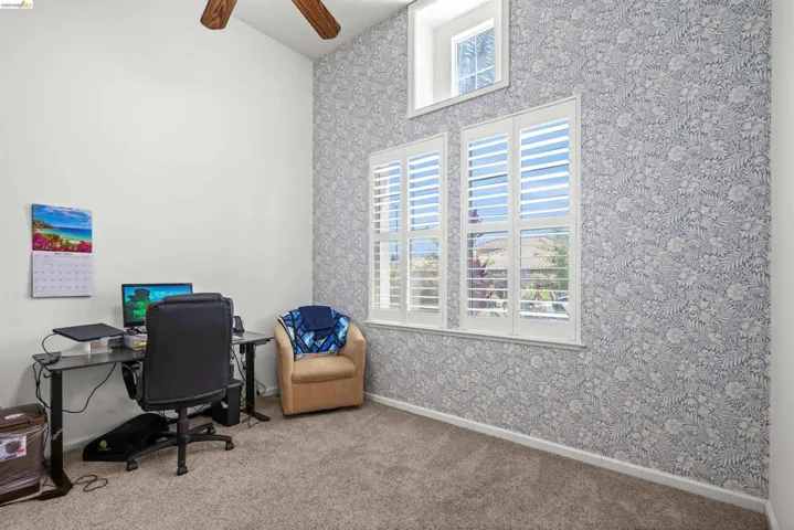 Vaulted ceiling room featuring a decorative accent wall, white window shutters, and a high transom window