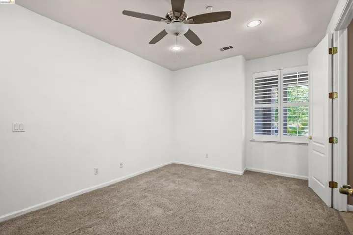 Carpeted room featuring a ceiling fan, recessed lighting, and a window with plantation shutters