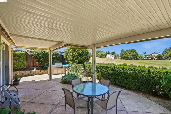 Expansive covered patio featuring a built-in barbecue station, a tiered water feature, and mature landscaping