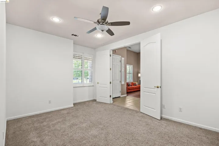 Carpeted interior space featuring a ceiling fan with integrated lighting, recessed ceiling lights, and plantation shutters on the window