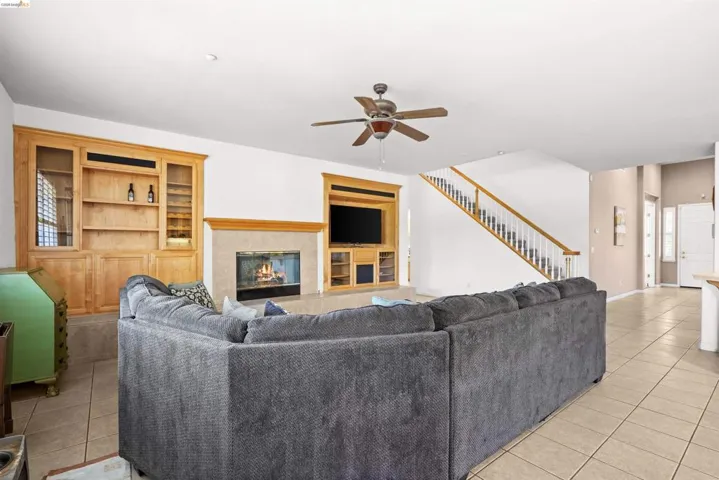 Living area featuring a fireplace with a stone surround, built-in media center, custom built-in cabinetry, tile flooring, and a ceiling fan