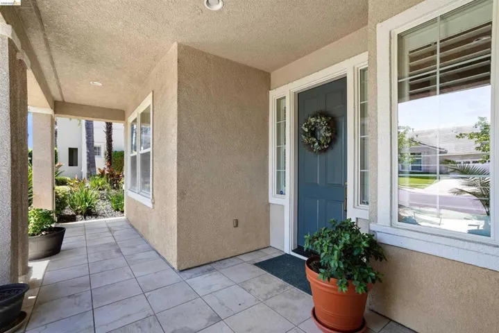 Covered front porch featuring large format tile flooring, stucco exterior, recessed lighting, and a paneled entry door with sidelights