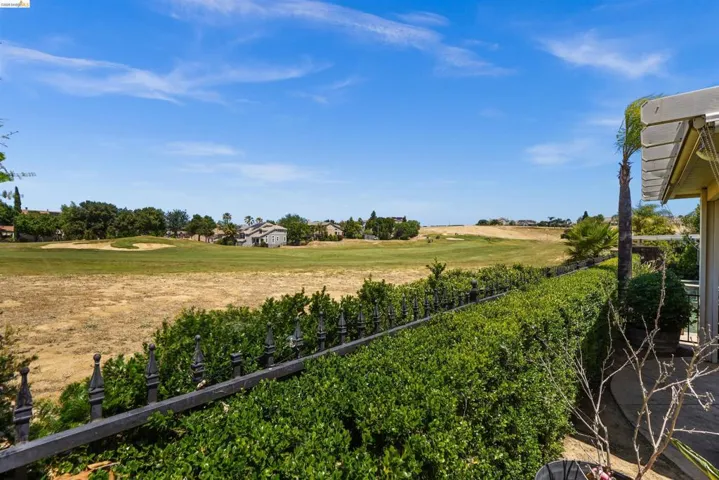 Expansive golf course terrain bordered by a manicured hedge and a decorative wrought iron fence