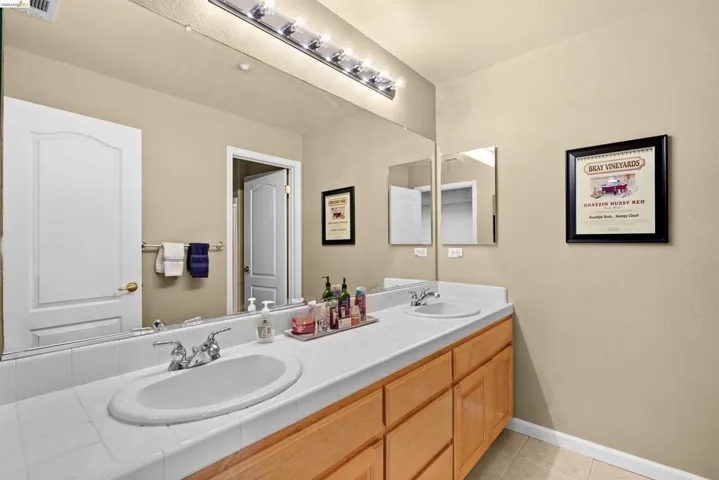 Double vanity featuring white tile countertop, dual undermount sinks, and chrome faucets