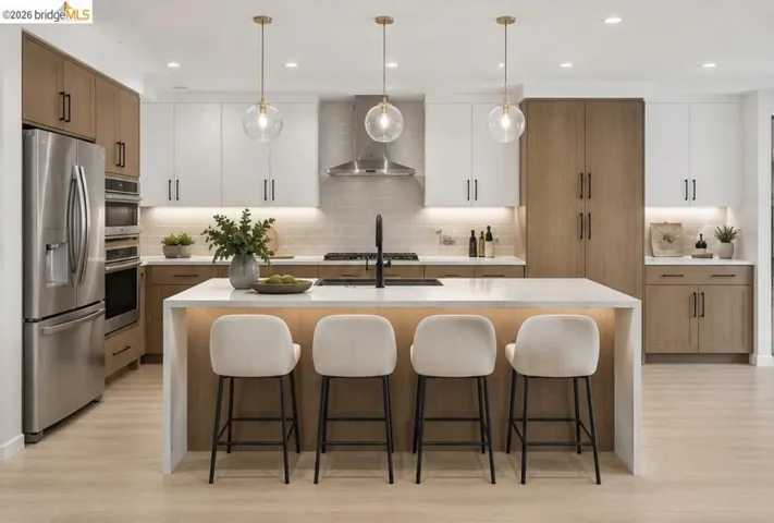 Open-concept kitchen featuring a waterfall island with counter seating, stainless steel appliances, two-tone cabinetry, and wood-finish flooring