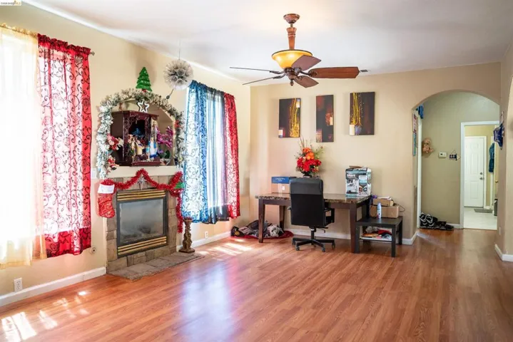 Living area featuring wood-finish flooring, a stone-surround fireplace, and an arched doorway