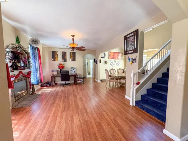 Spacious open-concept interior featuring wood-finish flooring, a stone-clad fireplace, and a ceiling fan with integrated lighting