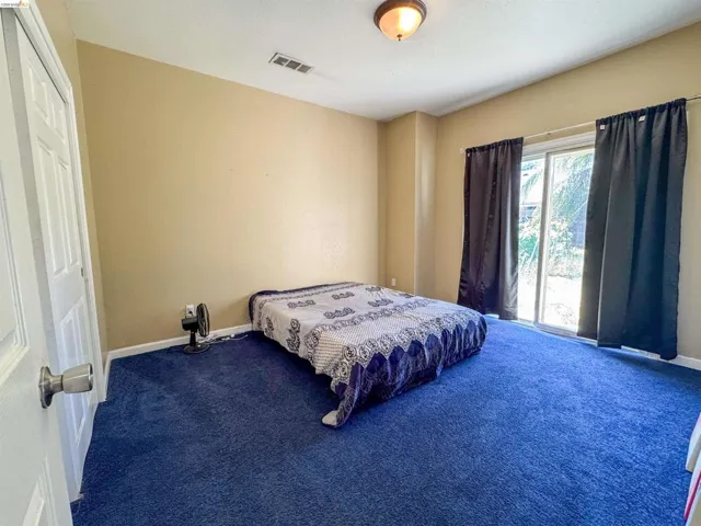 Spacious room featuring blue carpeting, neutral wall tones, and a sliding glass door providing natural light and exterior access