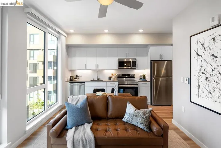 Open-concept living area featuring a kitchen with white cabinetry and stainless steel appliances, wood-finish flooring, a contemporary ceiling fan, and large windows