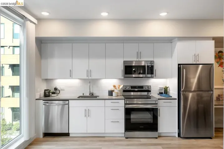 Modern kitchen featuring white cabinetry, stainless steel appliances, a subway tile backsplash, and light wood-finish flooring
