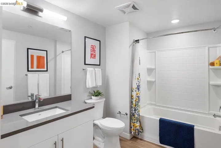 Contemporary bathroom featuring a vanity with an integrated sink and a dark countertop, a tub-shower combination with white subway tile surround, and wood-finish flooring