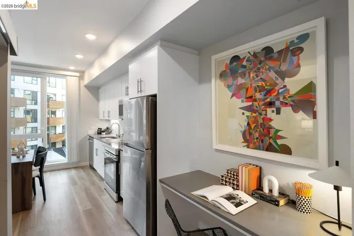 Kitchenette featuring stainless steel appliances, white cabinetry, recessed lighting, wood-finish flooring, and a large window
