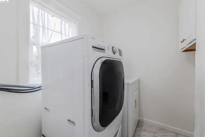 Washroom featuring washer / dryer, light marble finish floors, and cabinet space