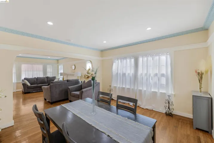 Dining space with arched walkways, light wood-style flooring, a raised ceiling, recessed lighting, and crown molding