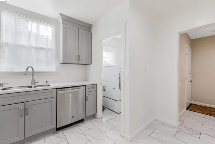 Kitchen featuring gray cabinetry, stainless steel dishwasher, washer / dryer, and light marble finish floors