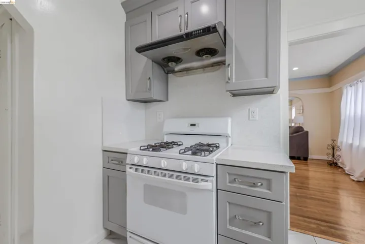 Kitchen with gray cabinets, gas range gas stove, under cabinet range hood, and light stone countertops