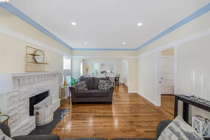 Living room with arched walkways, wood-type flooring, recessed lighting, ornamental molding, and a fireplace with flush hearth