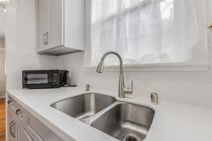 Kitchen with light stone counters, black microwave, and gray cabinetry