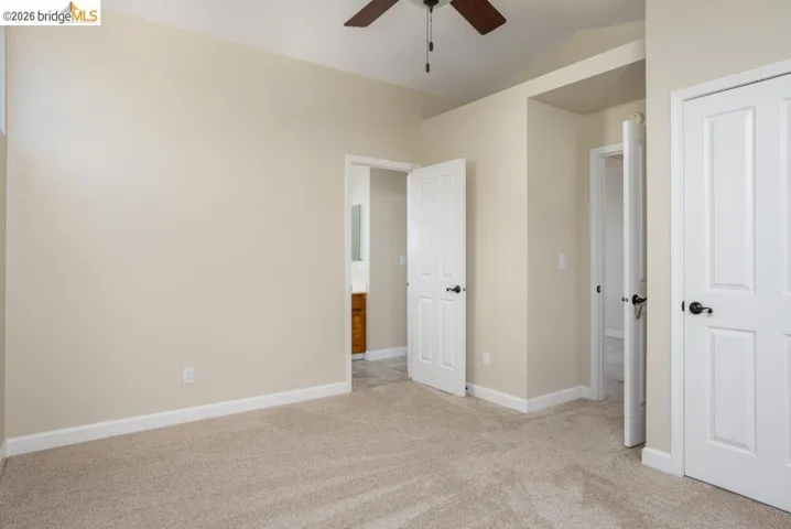 Neutral-toned wall paint and carpeting, overhead ceiling fan with light fixture, and multiple paneled doors