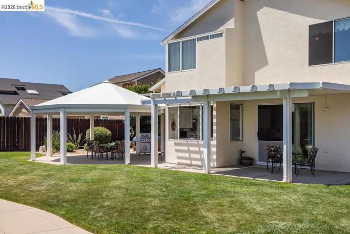 Expansive backyard featuring a lush lawn, concrete patio, and a standalone octagonal white pergola