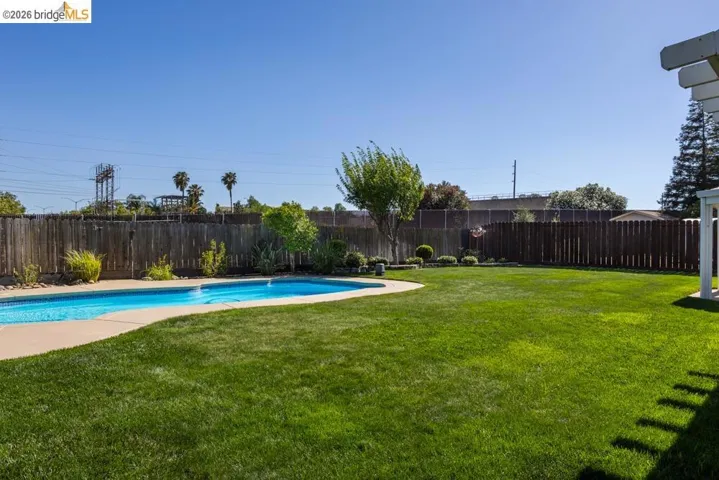 Expansive backyard featuring a large swimming pool with concrete surround, substantial lawn area, and mature perimeter fencing